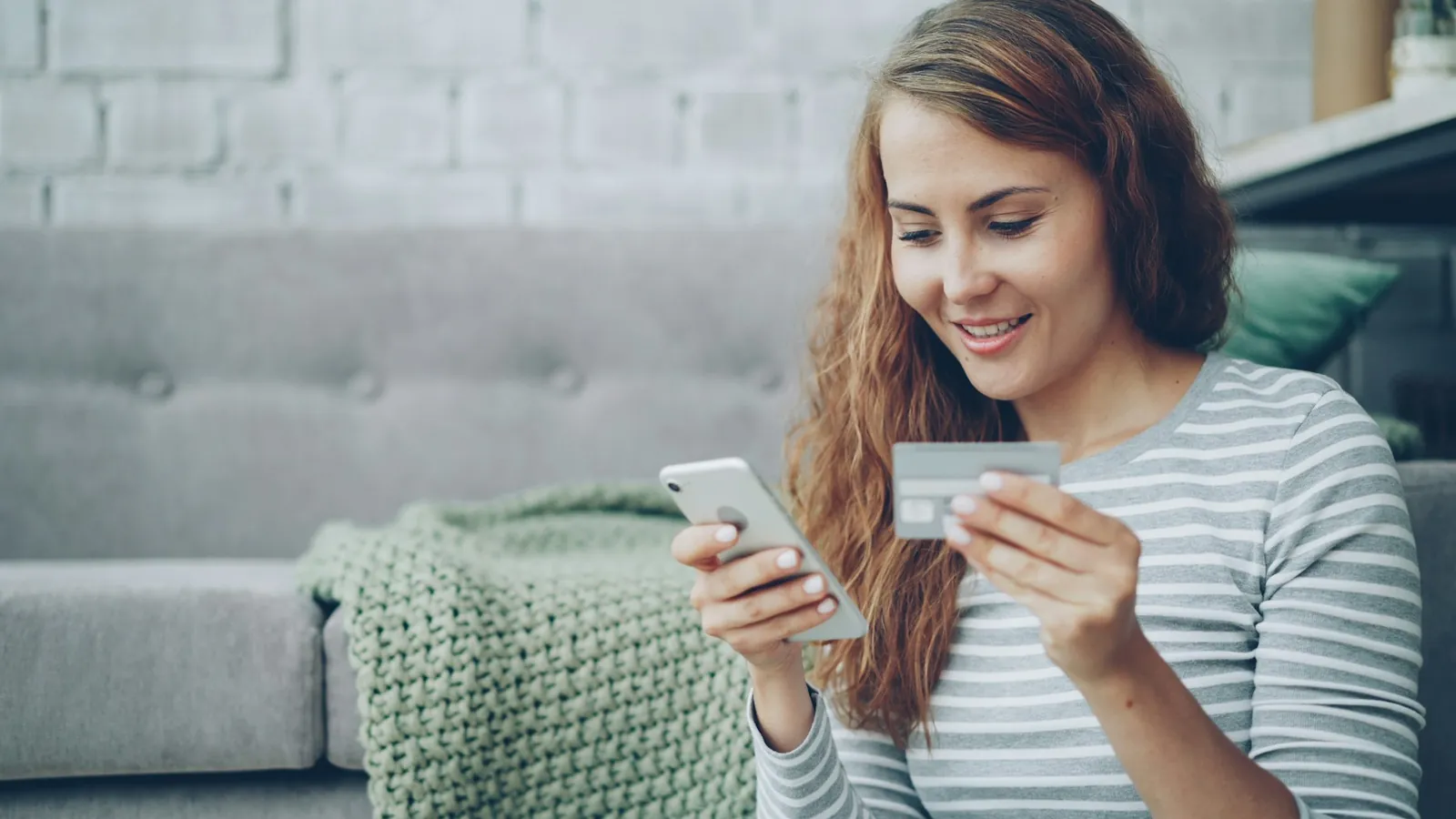 Pessoa paga uma compra pelo celular com um cartão na mão.