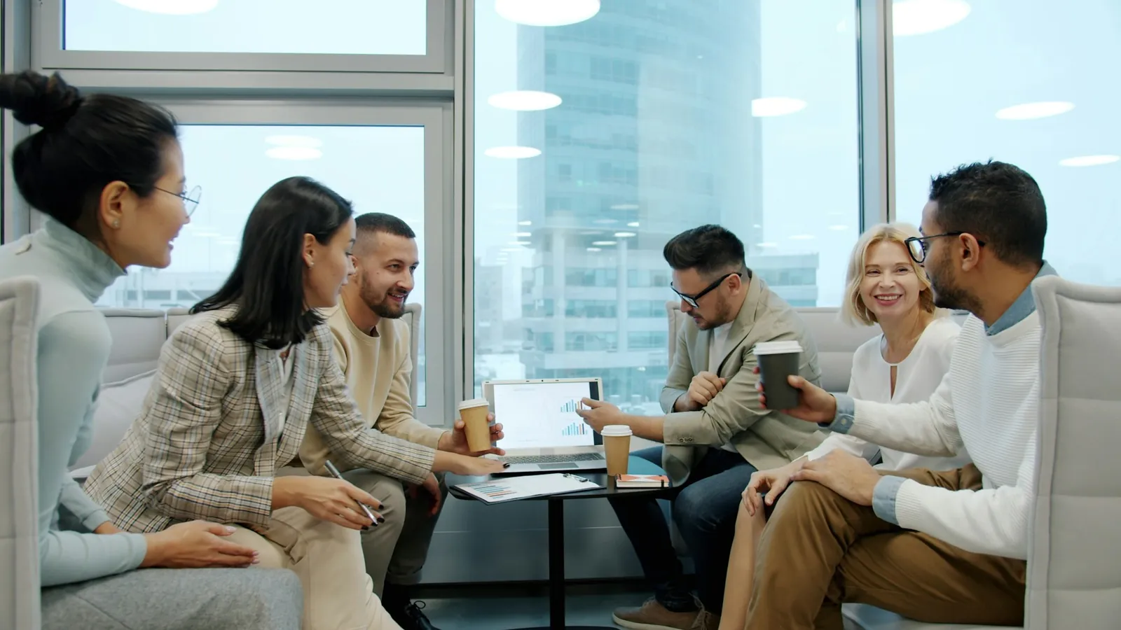 Equipe reunida em torno de uma mesa com notebook e café.
